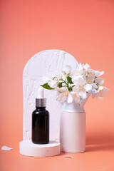 Cosmetic glass dropper bottle with oil, serum or fruit peeling on podium with jasmine flowers. Beauty product presentation on pink background. Front view. Mockup concept