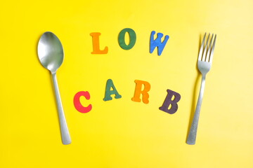 Low carb diet concept. Flat lay composition of low carbohydrates word text in plate with eating utensils spoon and fork in bright yellow background.