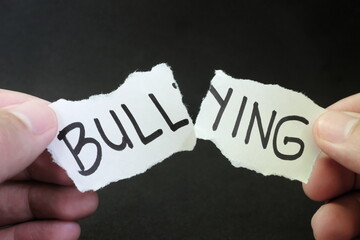 Fight and stop bullying concept. Hand tearing paper with word bullying in dark black background. - obrazy, fototapety, plakaty