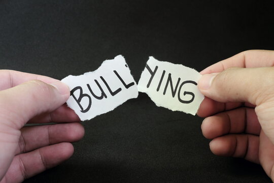 Fight and stop bullying concept. Hand tearing paper with word bullying in dark black background.