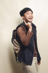 Fototapeta premium Portrait of Asian college young man pointing at empty space wearing brown t-shirt and black vest