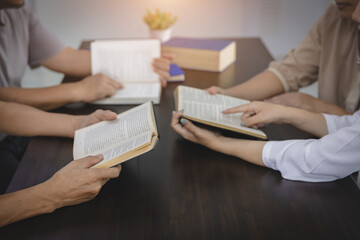 A group of Asian Christians sits inside a Catholic Church praying for God's blessing, the pale sun shining in the place of worship with copy space.