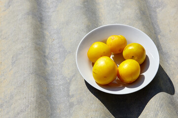 Ripe yellow plums on plate. Juicy fruit on wooden background, closeup. Fresh plum, vegetarian food. Harvest concept, top view