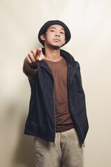 portrait of asian young man greeting his friend wearing hat, brown t-shirt and black vest isolated on background