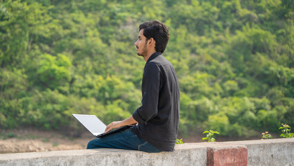 Young man working on a laptop and sitting in the nature, Workation and Digital Nomad concept.