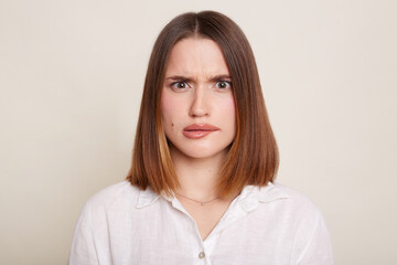 Portrait of dark haired Caucasian attractive woman wearing shirt posing isolated over white background, looking at camera with frowning face, being confused. - obrazy, fototapety, plakaty