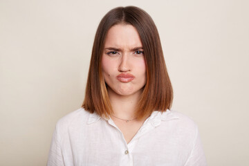 Image of Caucasian dark haired attractive woman wearing shirt, looking at camera with pout lips, being sad and confused, posing isolated over white background.