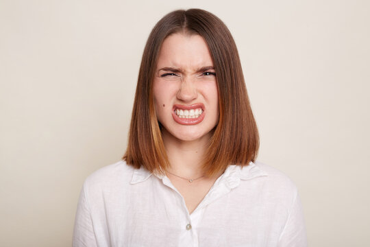 Portrait of Caucasian angry Caucasian woman wearing shirt posing isolated over white background, aggressive emotions, looking at camera with clenched teeth.