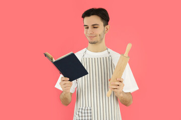 Concept of cooking, young man in apron on pink background