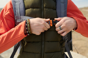 Cropped shot of unrecognizable female tourist standing outdoors adjusting chest belt on hiking...
