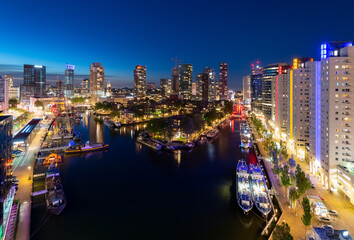 Rotterdam “Leuvehaven“ harbour panorama at evening blue hour on river Maas in South Holland Netherlands. Reflections of modern buildings and colorful lights and illumination. Boats and vessels moored.