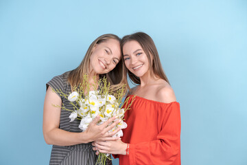 Happy women's day. Beloved daughter congratulates her mother and gives her beautiful flowers in a bouquet. Mom and girl smile and hug on a blue background. Family holiday and unity.