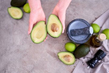 Closeup on hands holding fresh avocado cut in half over grey concrete table