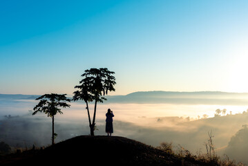 Silhouette woman standing on the top of mountain with sunrise landscape, mist and fog  in morning .