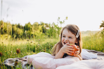 Cute little girl picking up apples in a green grass background at sunny day