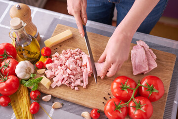 woman's hands slicing pancetta ham bacon on wooden cutting board at domestic kitchen