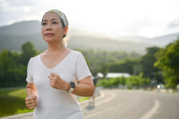 Sporty asian aged woman running jogging in a summer day in the beautiful park.