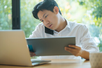 Asian man working busy while making phone call and using laptop at home