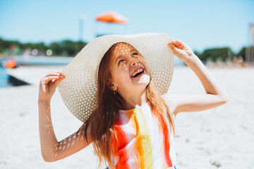 Portrait of a beautiful little girl in a striped dress and a straw hat sitting on the beach