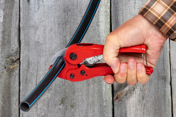 Craftsman tools. A man accurately cuts a piece of PE pressure pipe or water pipe with a red pvc...