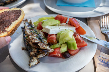 Grilled fish sardines. Freshly fish served with Greece salad in white plate. Gourmet seafood dinner in outdoor restaurant, taverna in Crete, Greece cuisine. Healthy lifestyle concept.