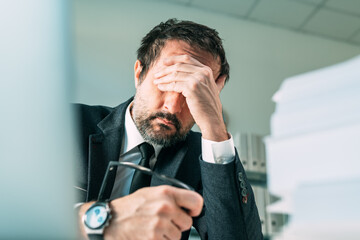 Overworked businessman at office desk, tired fatigued business owner in stressful situation