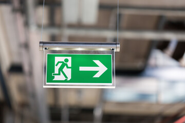 Illuminated emergency exit sign, hanging from the ceiling. With running figure and an arrow which points to the right. - obrazy, fototapety, plakaty