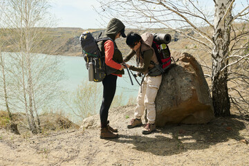 Young Asian woman helping her friend to fix and adjust backpack after having break during hiking around quarry lake