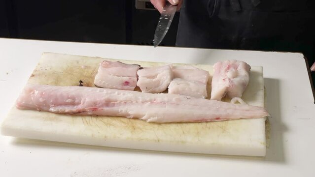 Hands close up of professional man cook cutting raw hake ish in Spanish restaurant before baking it for dinner