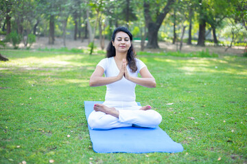 Fototapeta premium Beautiful indian woman doing breathing yoga exercise in the park, Asian female meditation pose, healthcare.