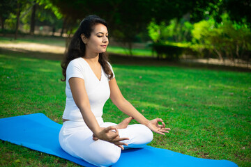 Beautiful indian woman doing breathing yoga exercise in the park, Asian female meditation pose, healthcare.