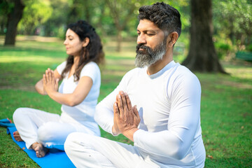 Indian people doing yoga exercise in the park, Asian man and woman do meditation pose, healthcare....