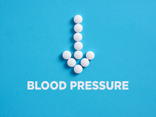 Round white medical pills in arrow shape pointing to the word blood pressure. Reducing blood...