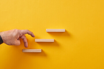 Male hand climbing the wooden cube stairs on yellow background. Career goal achievement, business success and development
