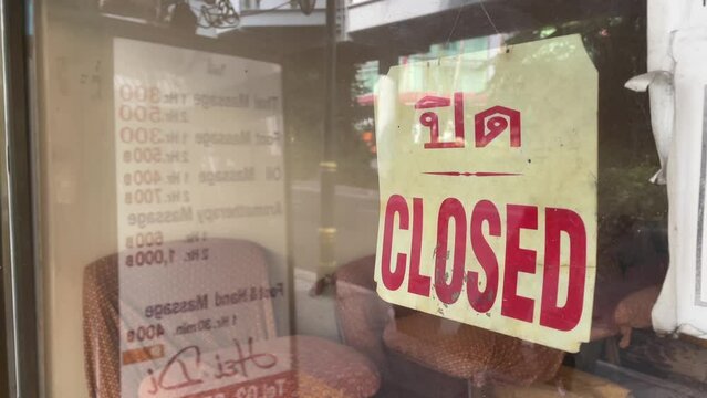 Closed sign on window glass at storefront with traffic on road - day 