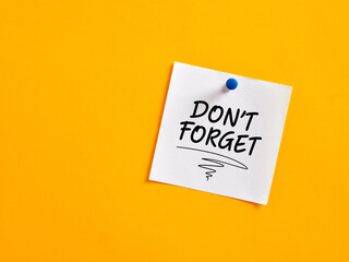 The notice reminder don't forget written on a note paper pinned on a yellow board.