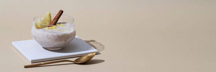 Spanish dessert arroz con leche or creamy rice pudding with Cinnamon and lemon on beige background. Banner with copy space