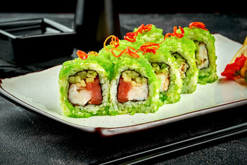 Sushi roll with salmon and shrimp with cucumber in green caviar in a white plate