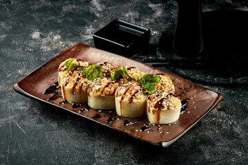Baked roll with eel and unagi sauce in a brown plate