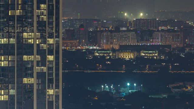 Buildings around Deira and creek district in Dubai night timelapse. Tall towers with glowing windows and city skyline aerial view. Dubai, UAE.