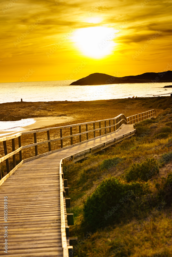 Wall mural Sunset over beach with wooden path to sea water.