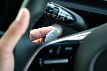 Action of driver's hand is controlling gear paddle shift on the car steering wheel. Close-up and selective focus. - obrazy, fototapety, plakaty