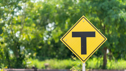 Intersection traffic sign on the metal signboard with background of greenery tree. Transportation symbol object photo.