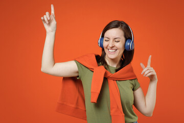 Young smiling happy fun woman 20s wear khaki t-shirt tied sweater on shoulders headphones listen to...