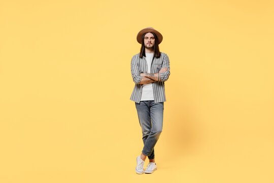 Full body young smiling man he 20s wears striped grey shirt white t-shirt hat look camera hold hands crossed folded isolated on plain yellow color background studio portrait. People lifestyle concept.