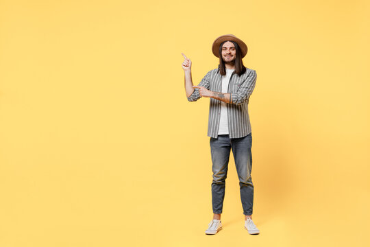 Full body happy young man he 20s in striped grey shirt white t-shirt hat pointing index finger aside indicate on workspace area copy space mock up isolated on plain yellow background studio portrait