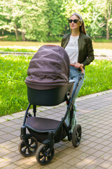 A stylish mom walks with a child who sleeps in a stroller. Walking in the fresh air of the park