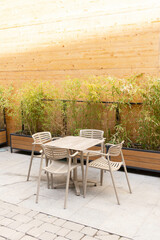 Table and chairs in a street with a wall of wooden planks and plants