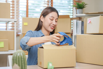 Small business entrepreneur SME, asian young woman,girl owner packing product, checking parcel for delivery to customer, using scotch tape to seal the box, working at home. Merchant online, e commerce