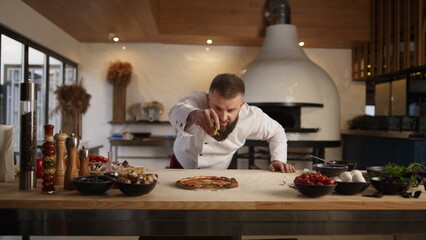 Man cooking pizza in italian food restaurant. Chef adding ingredients on pastry.